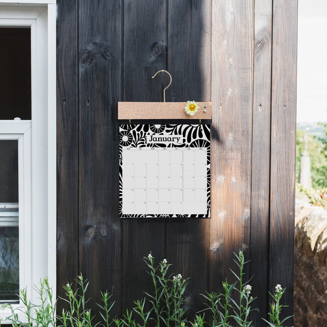 Calendar with monochrome floral design attached to a wooden wall outdoors.
