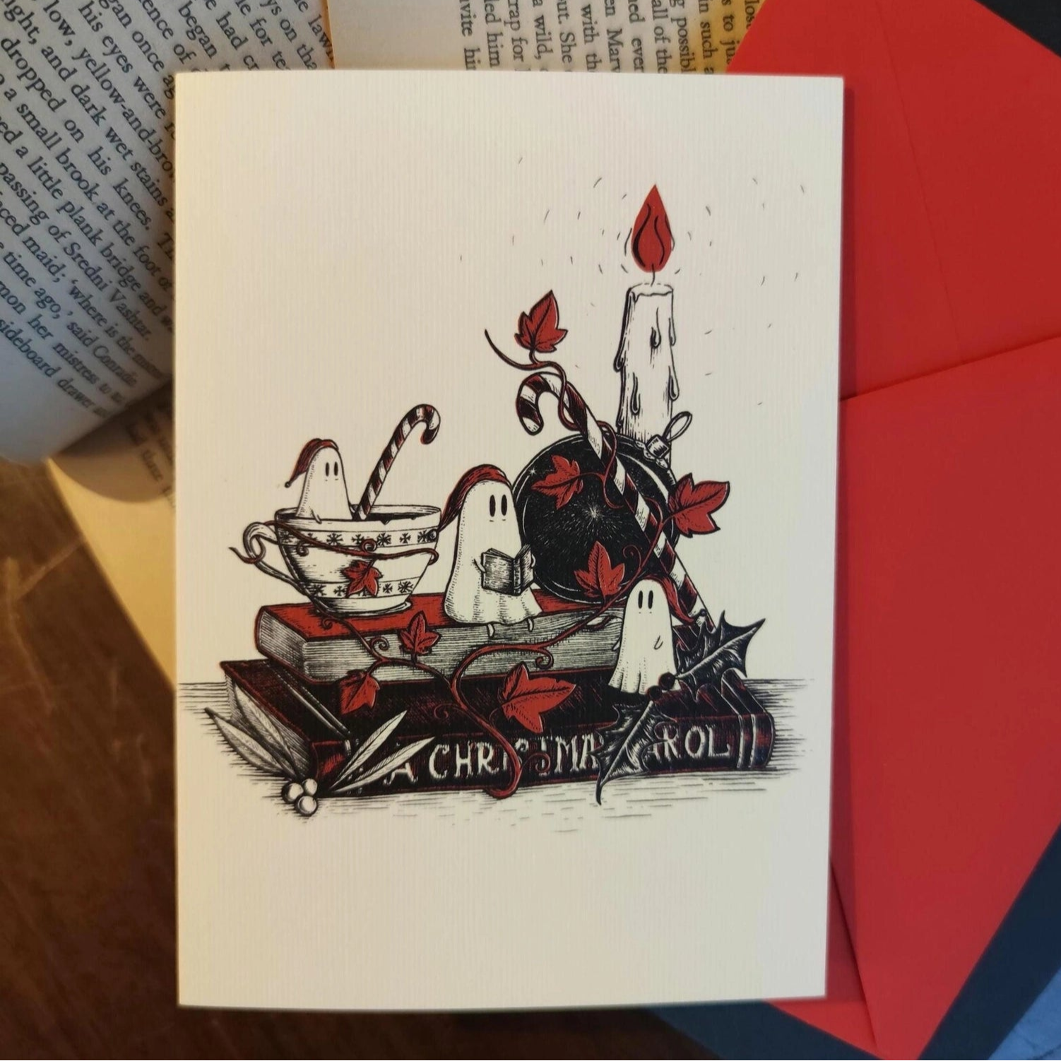 White Christmas card with nightcapped ghosts sat on a copy of A Christmas Carol, by candleight.