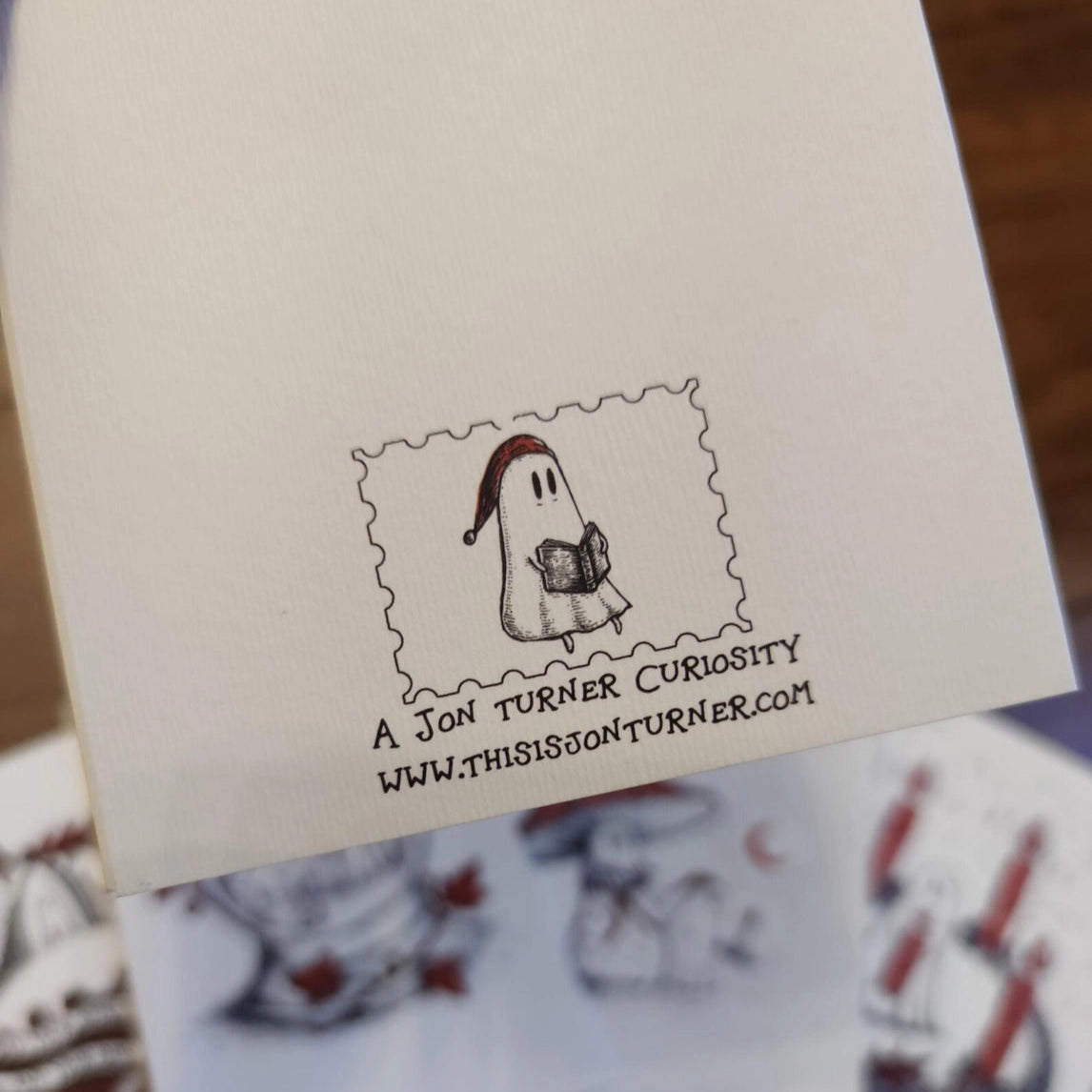 The back of a card,  with a stamp themed ghost illustration and text on a wooden surface