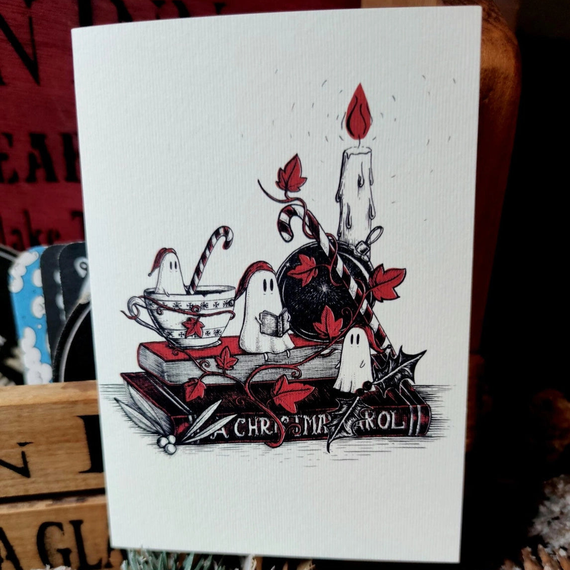 Christmas greeting card with Halloween-themed design featuring ghosts, a candle, and text on a textured surface.