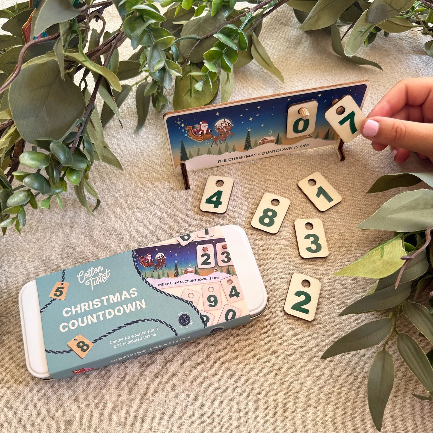 Christmas countdown calendar with numbered tiles on a textured surface with green leaves.