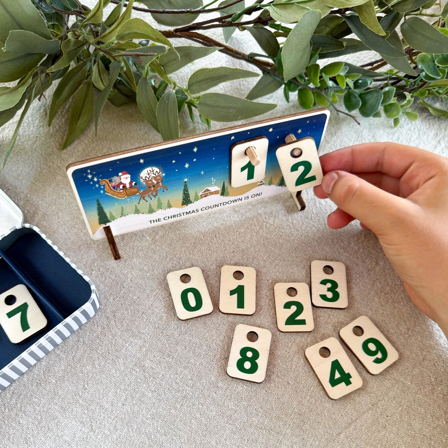 Christmas countdown calendar with wooden number tags on a textured surface with greenery.