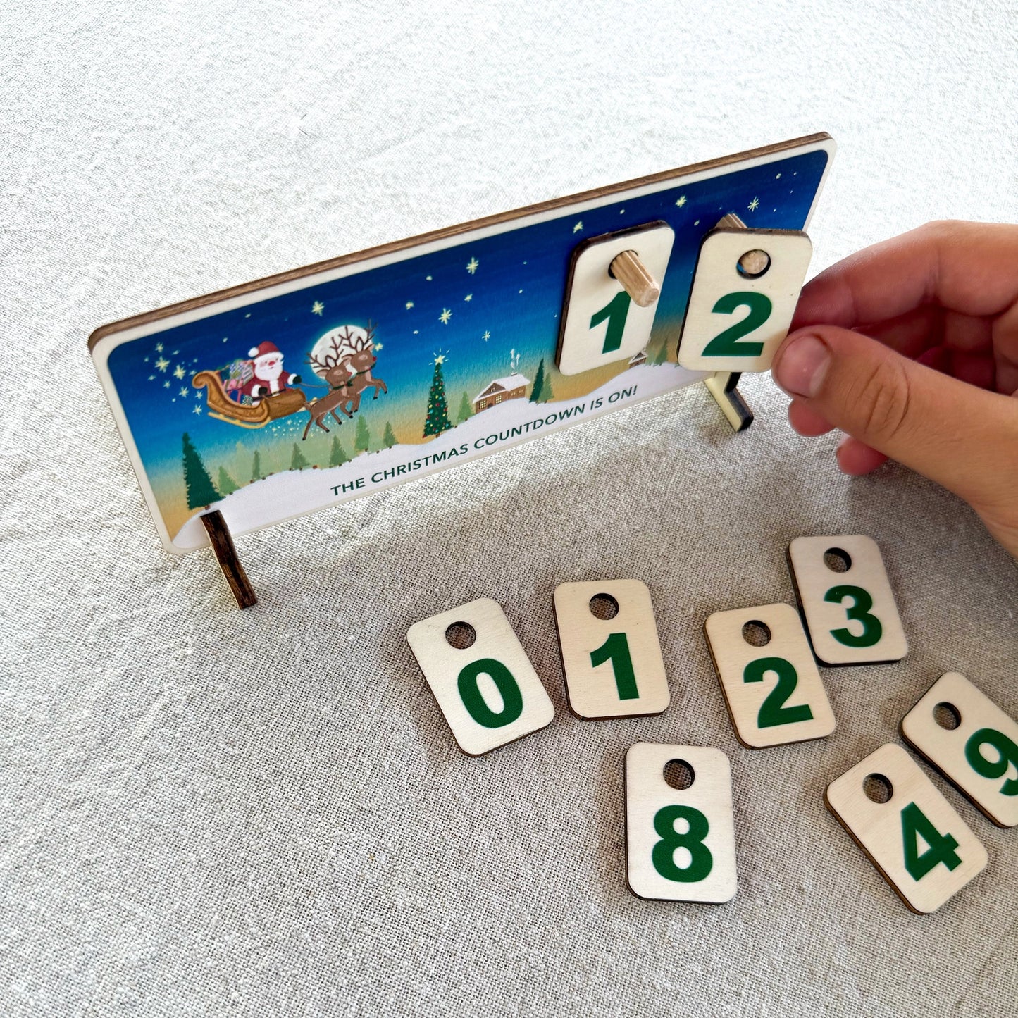 Hand setting a wooden number on a Christmas-themed advent calendar.