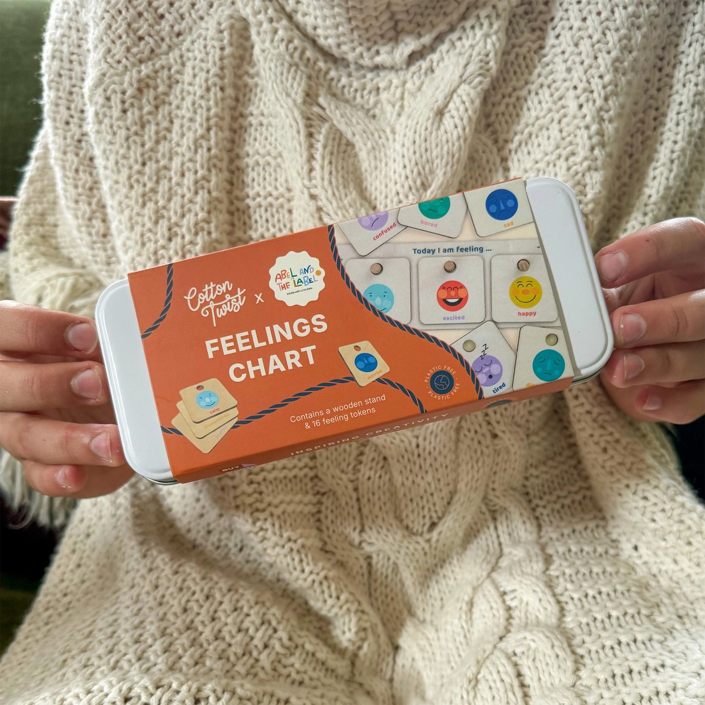 Person holding a feelings chart packaging with a textured beige sweater background