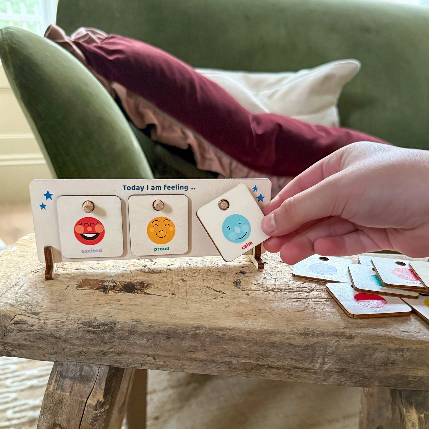 Hand holding a set of emotion cards on a wooden surface with a green couch in the background