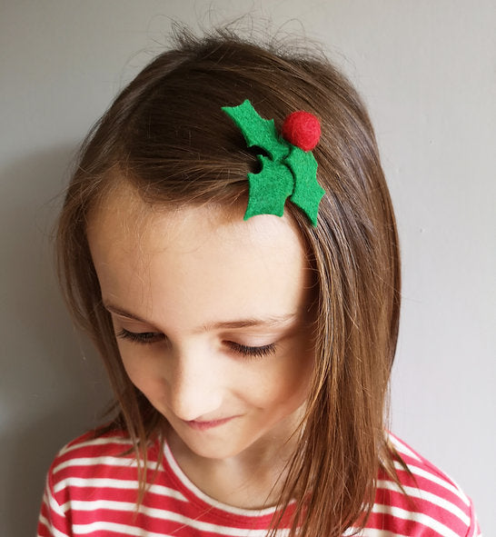 Child wearing a festive hair clip with green leaves and a red berry on a plain background