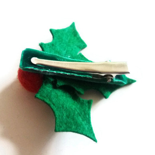 The reverse side of a green holly leaf hair clip with a red berry on a white background.