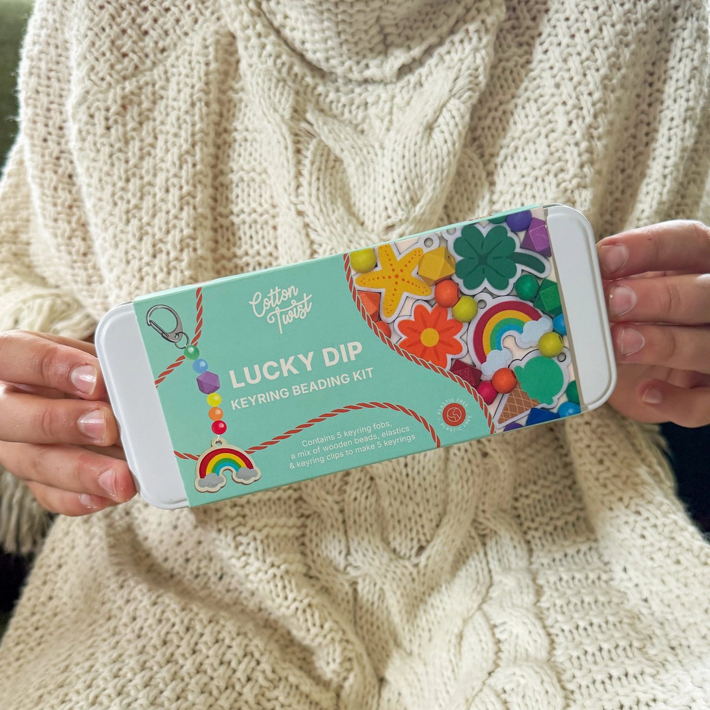 Person holding a 'Lucky Dip' keyring beading kit packaging against a beige sweater background