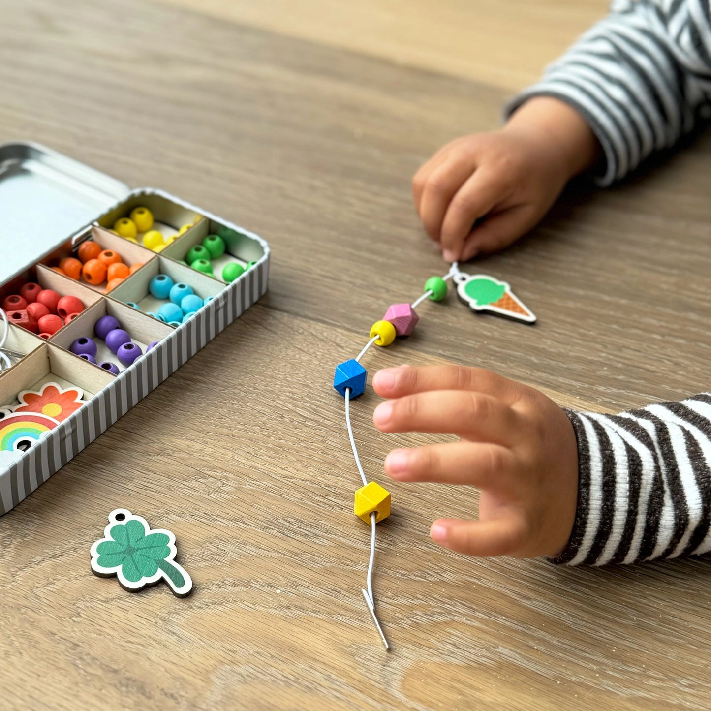Child's hands playing with colorful beads and charms on a wooden table