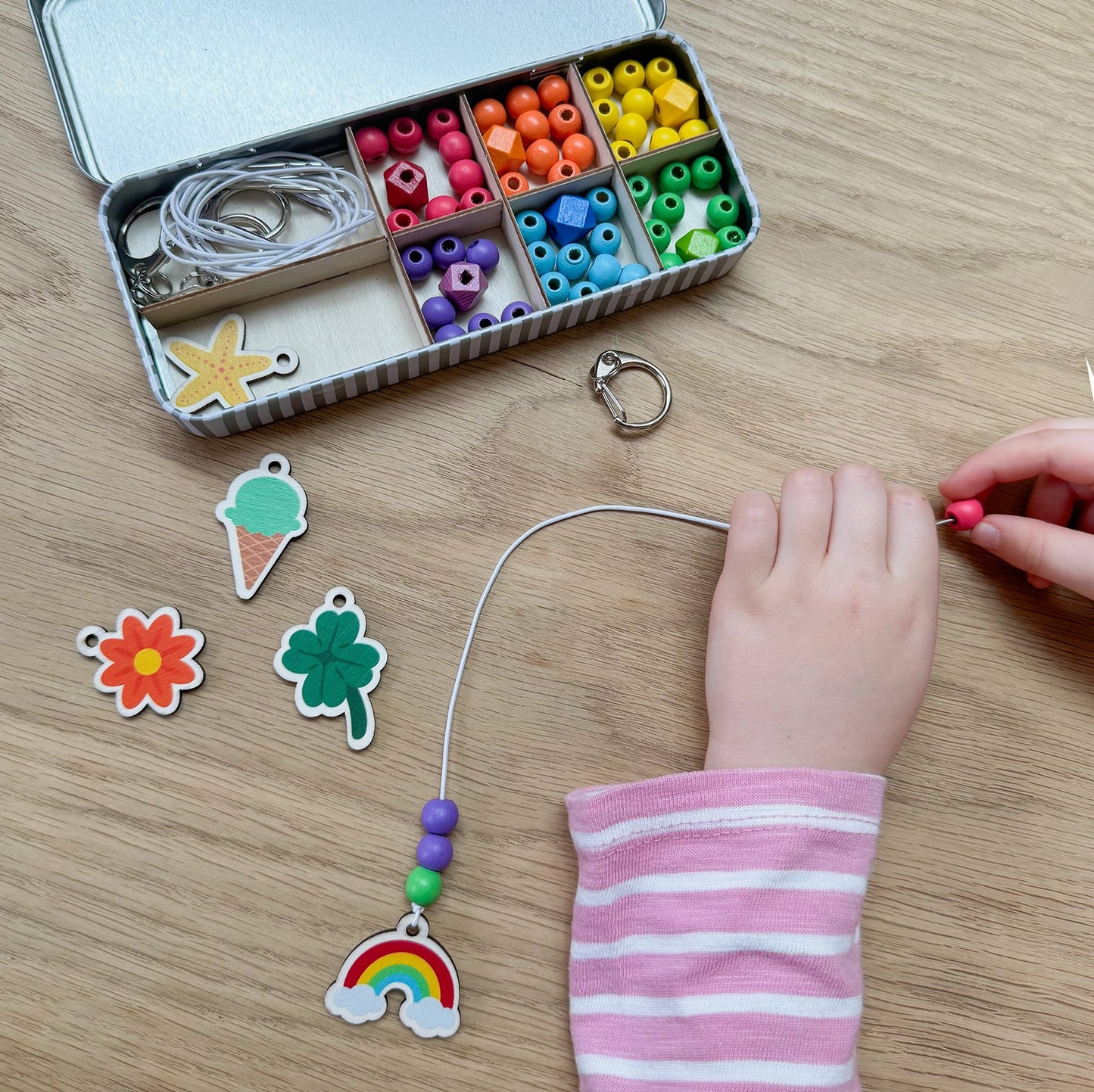 Child's hand working with colorful beads and charms on a wooden table