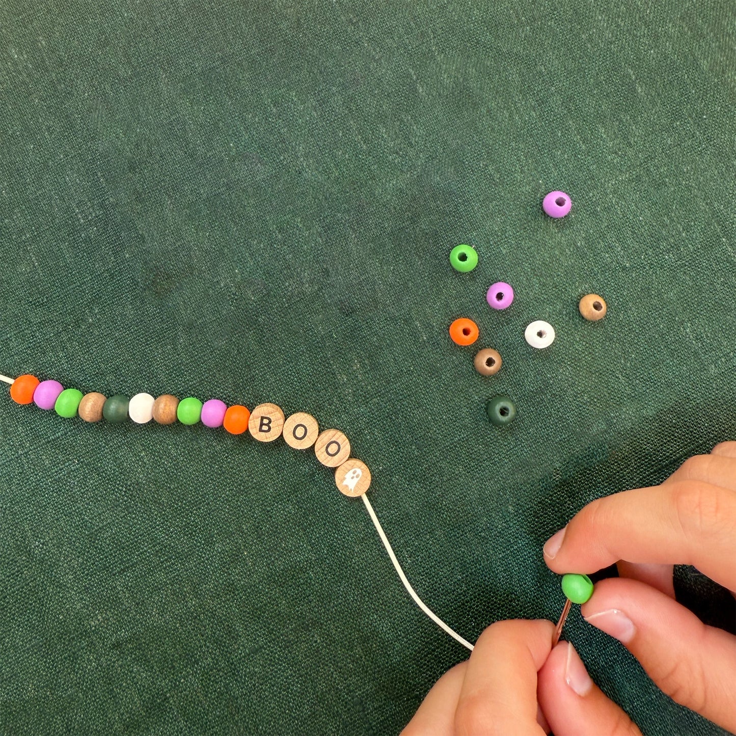 Person stringing colorful beads on a green fabric background