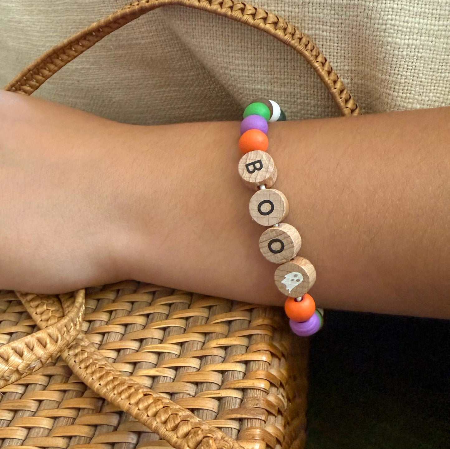 Bracelet with wooden beads spelling 'BOO' on a wrist against a woven background