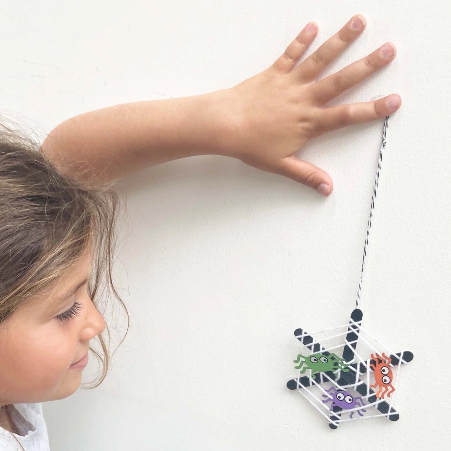 Child playing with a spider web toy on a white surface