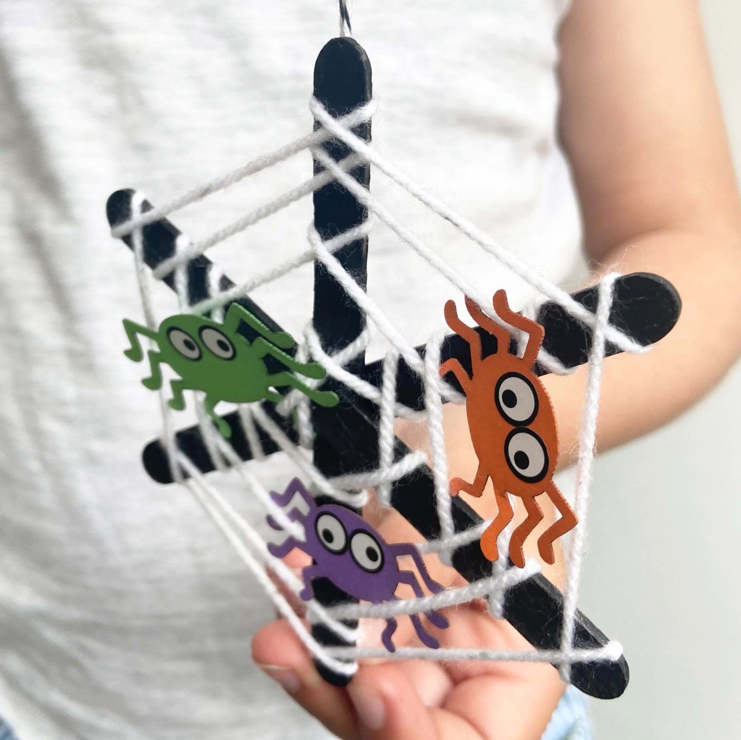 Hand holding a spider web with colorful spider decorations against a white background