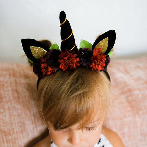 Child wearing a decorative headband with black horn, ears and flowers on a neutral background