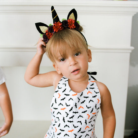 Child wearing a Halloween-themed headband and dress with bat pattern.
