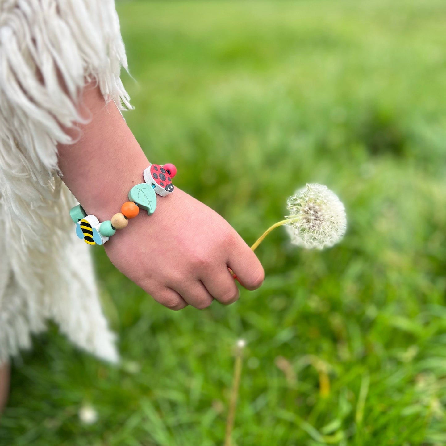 Child's hand holding a dandelion with a colorful bracelet on a grassy background