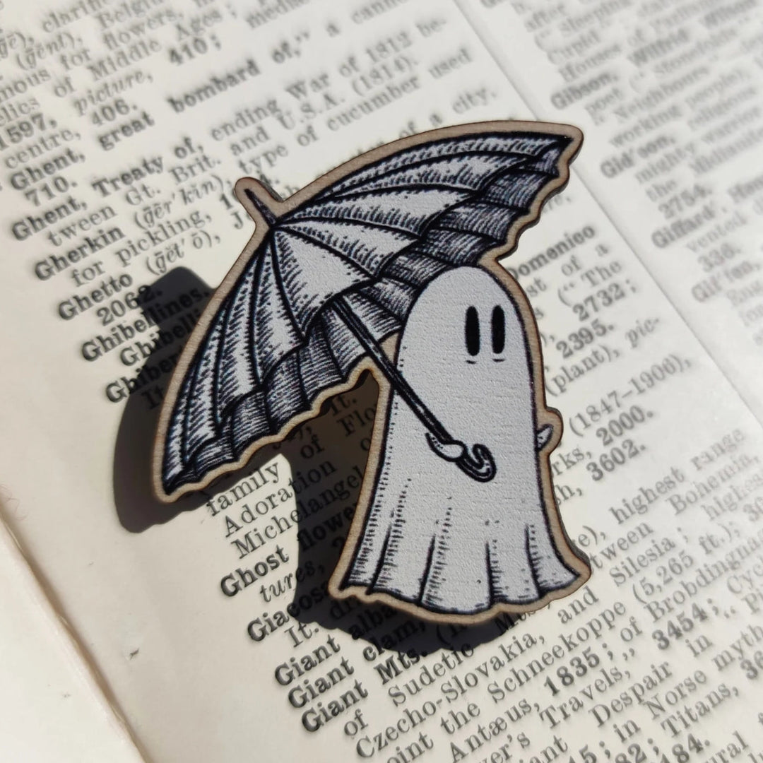 Black and white ghost with an umbrella wooden pin, sat on a book page.