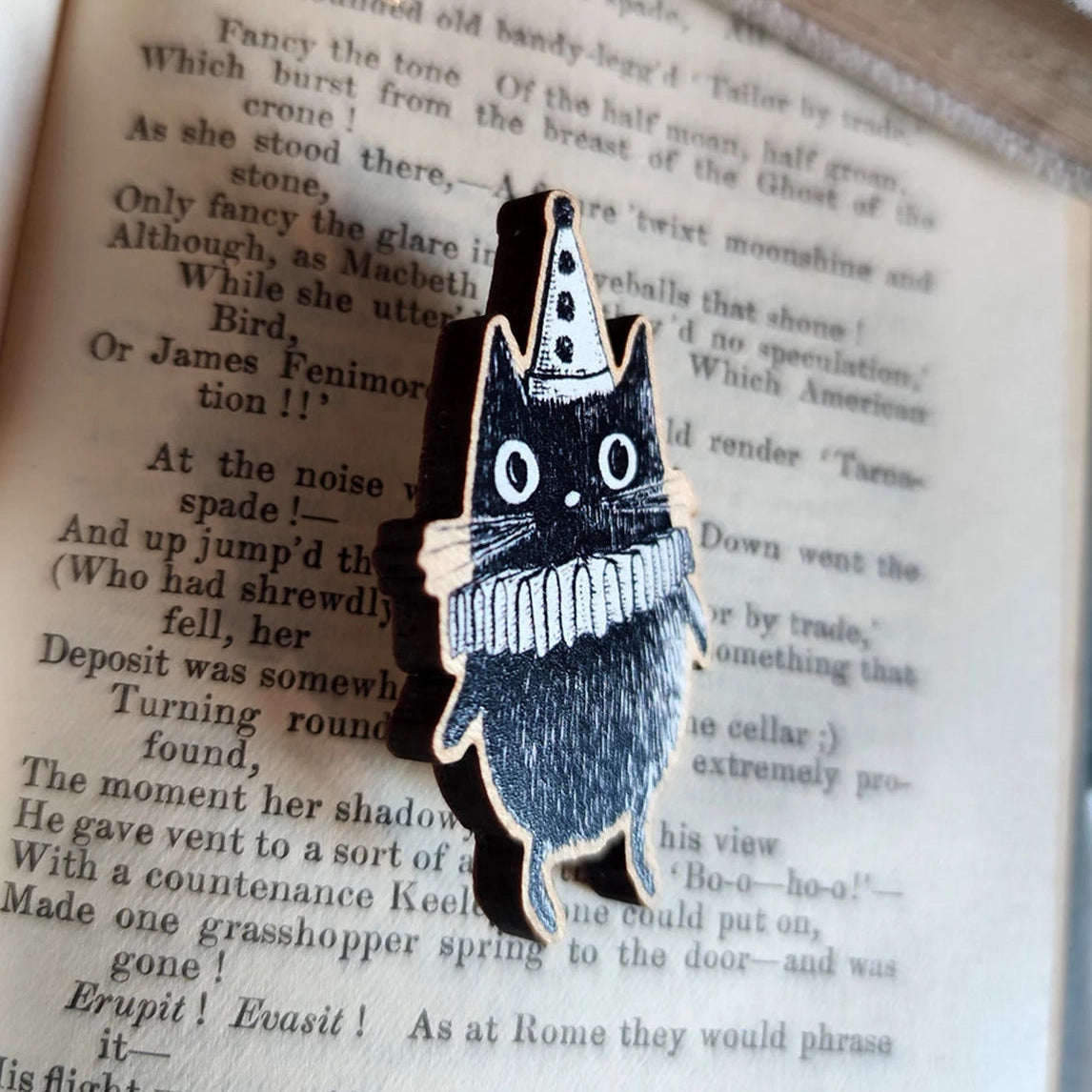 Black and white clown cat pin badge, sideways on. Sat on an open book.