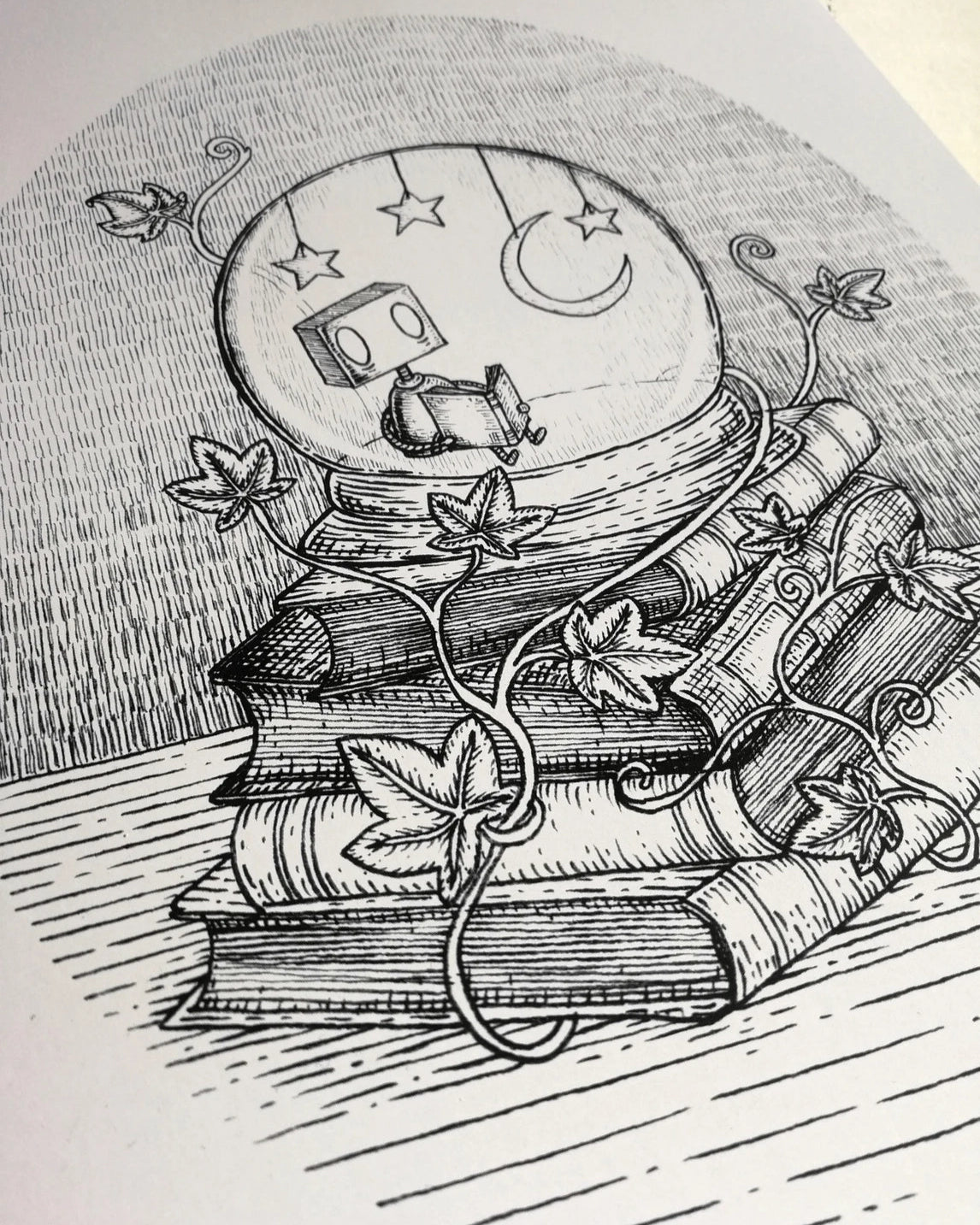 Closeup of a black and white illustrated art print, featuring a small robot reading in a moonlit snowglobe.