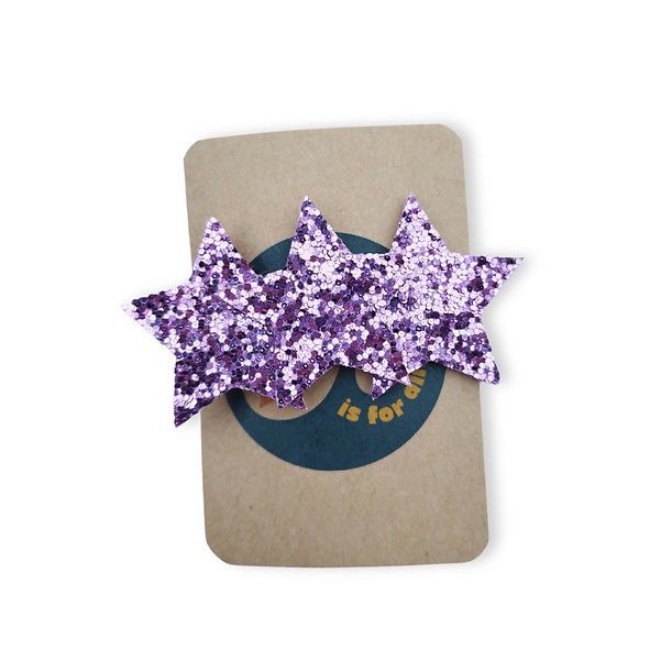 Brown backing card holding a sparkly purple hairclip in the shape of 3 stars.