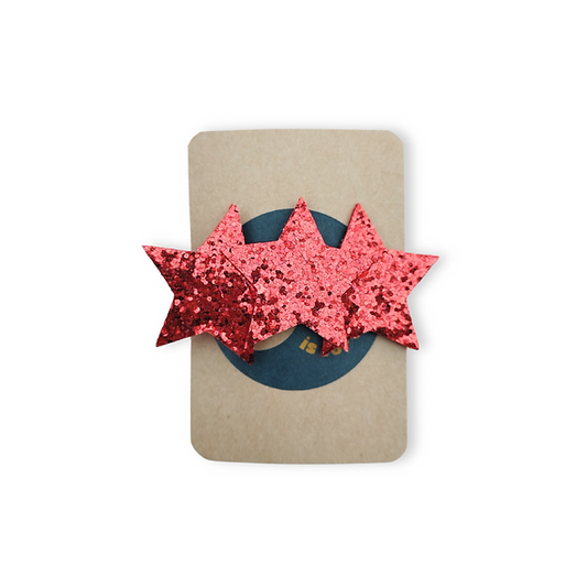 Brown backing card holding a sparkly red hairclip in the shape of 3 stars.