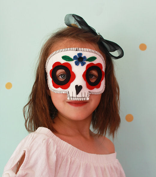 Child wearing a colorful skull mask with floral details on a light blue background
