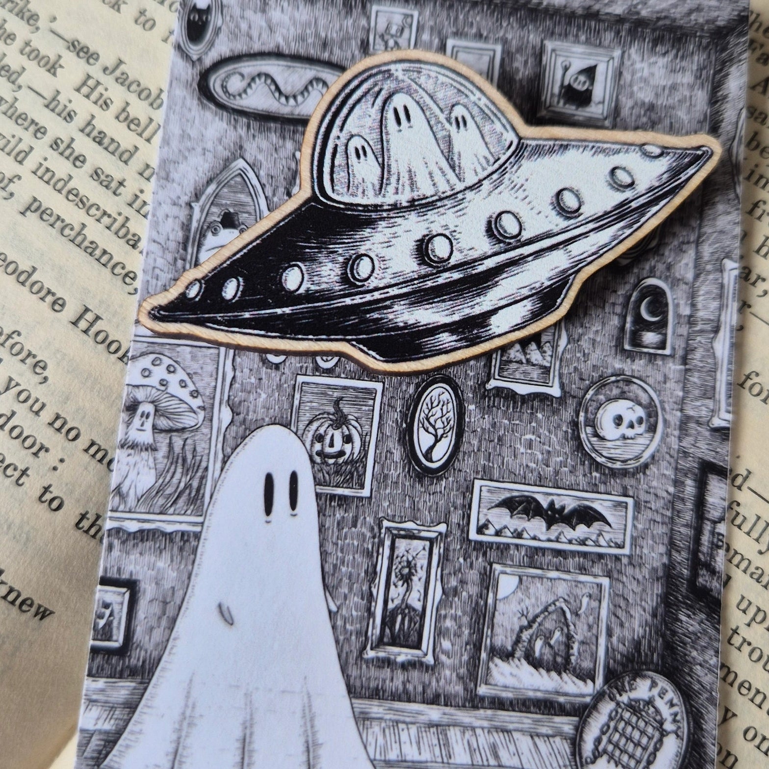 A woonden pin badge with a black and white design, featuring a flying UFO with ghosts inside. Pin is on an illustrated backing card.
