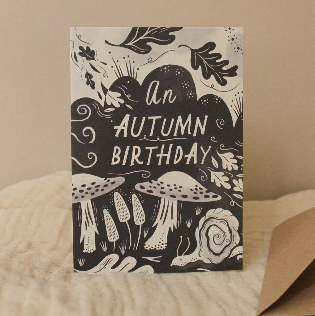 Greeting card with 'An Autumn Birthday' text and autumn-themed illustrations on a beige background.