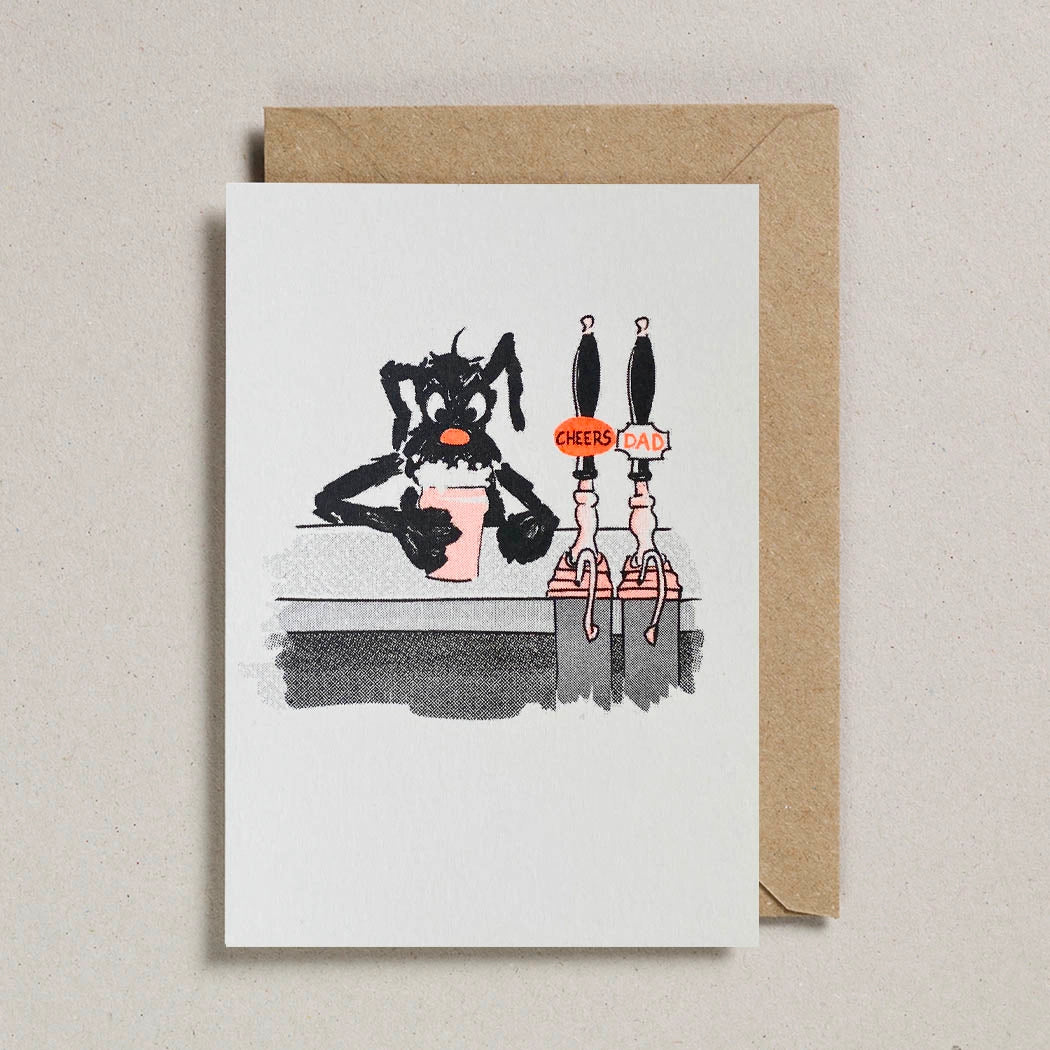 Comic inspired image of a dog sat at a bar drinking a pint, next to beer pumps with teh words 'Cheers Dad'. A white card with brown envelope on a beige background.