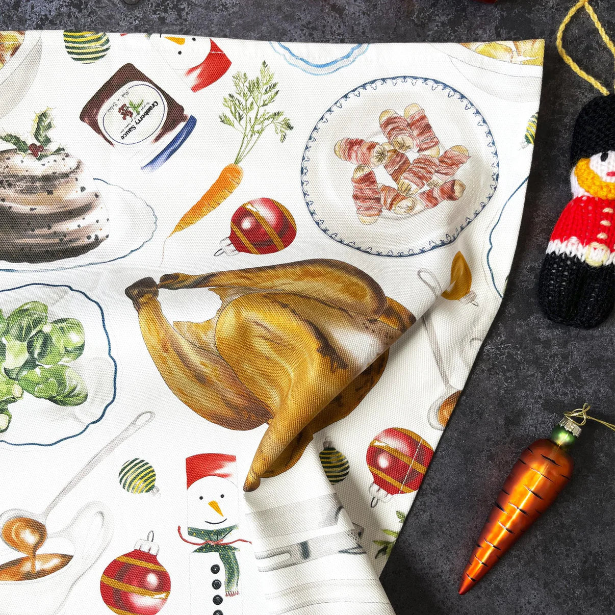 Closeup of tea towel with festive food illustrations and a black surface with a carrot tree decoration.