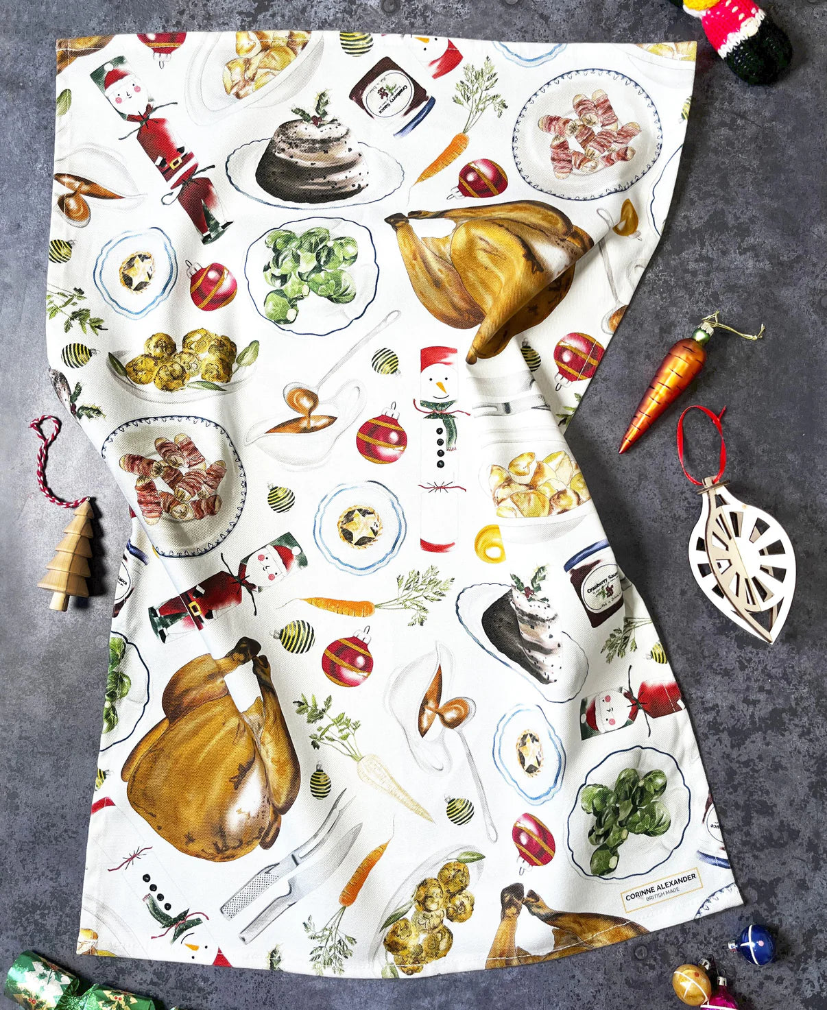 Christmas tea towel with festive food illustrations laid flat on a grey surface.