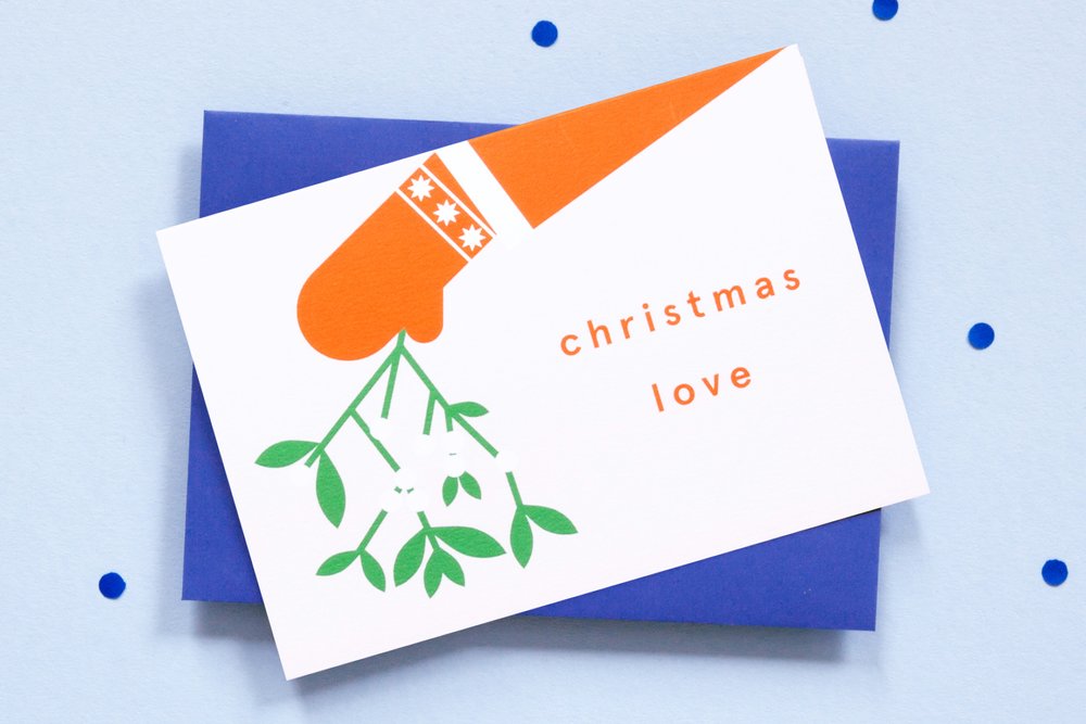 White card with red chirtmas mitten and coat sleev holding mistletoe with the words Christmas Love. Bold colours in a minimalist design. Blue envelope.