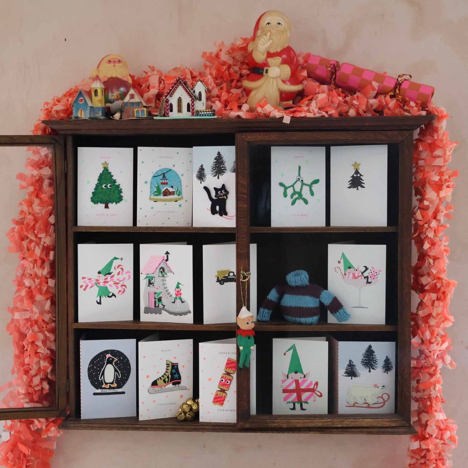 Wooden shelf with Christmas-themed cards and decorations against a pink floral background
