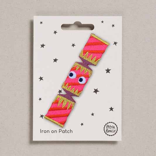 Iron on patch with a pink Christmas cracker design with googly eyes. On a beige background.