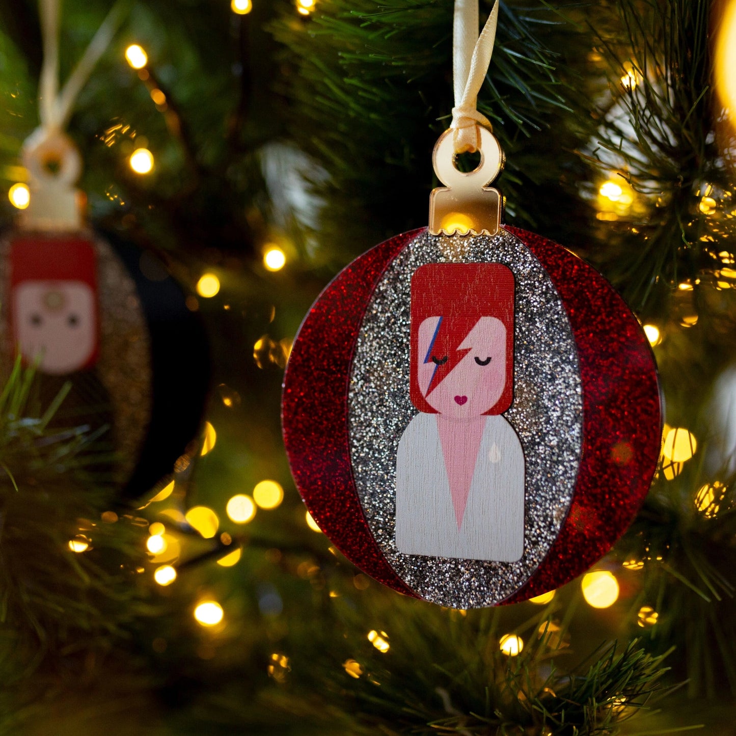 Red & silver glittery acrylic David Bowie / Aladdin Sane bauble hanging in a Christmas tree. 