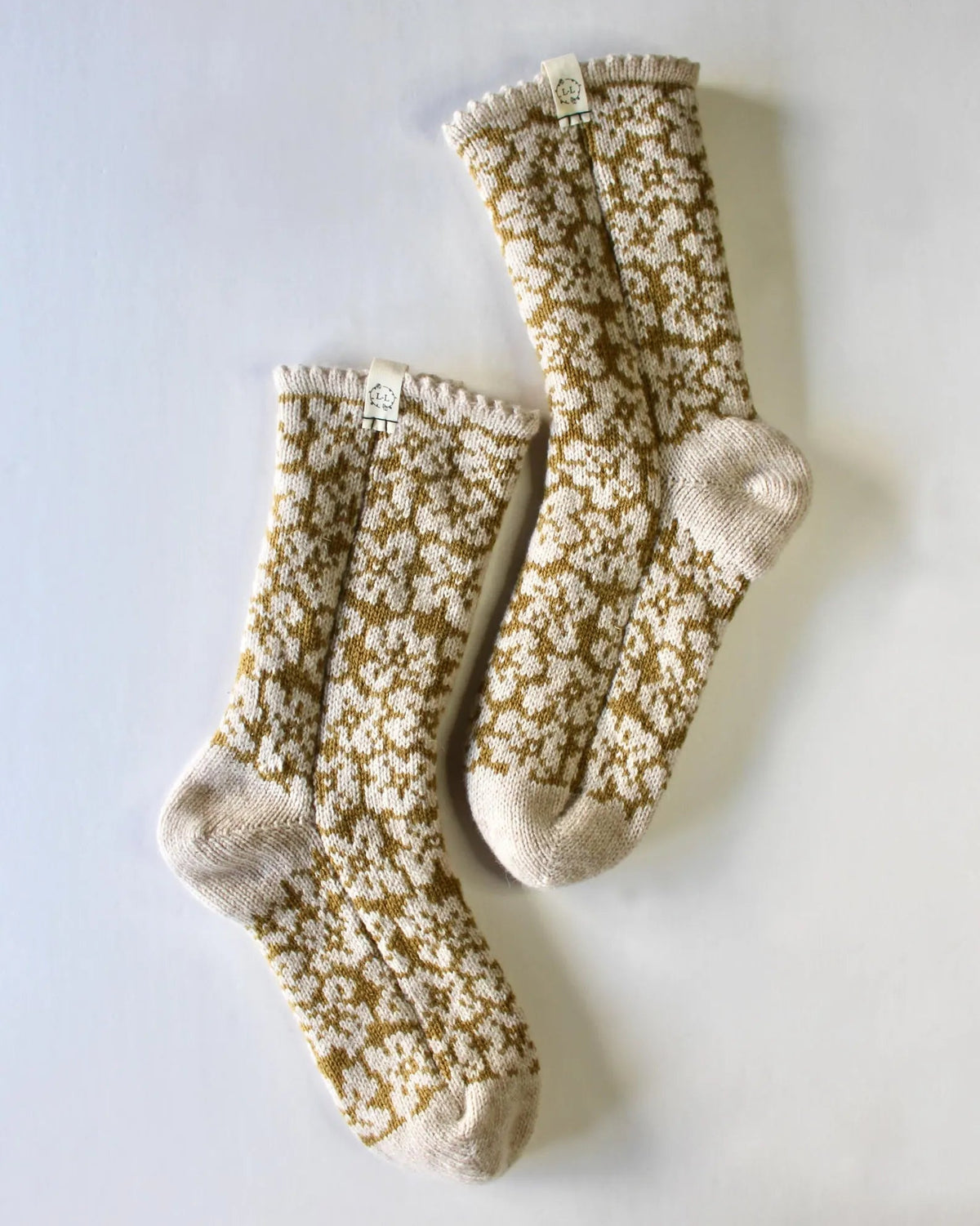 A pair of cream and mustard yellow floral patterned bed socks with cuffs, laid flat on a light gray background.
