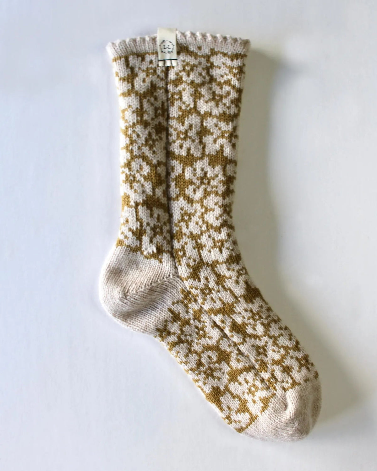 A single knitted bed sock with a cream and mustard yellow floral pattern, shown against a plain light gray background.