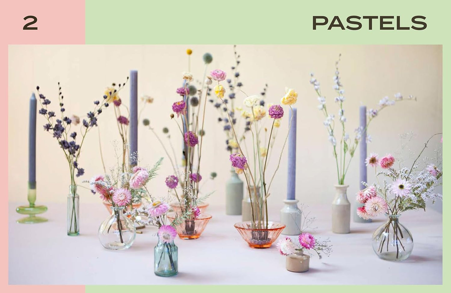 Decorative arrangement of flowers and candles in pastel colors on a neutral background.