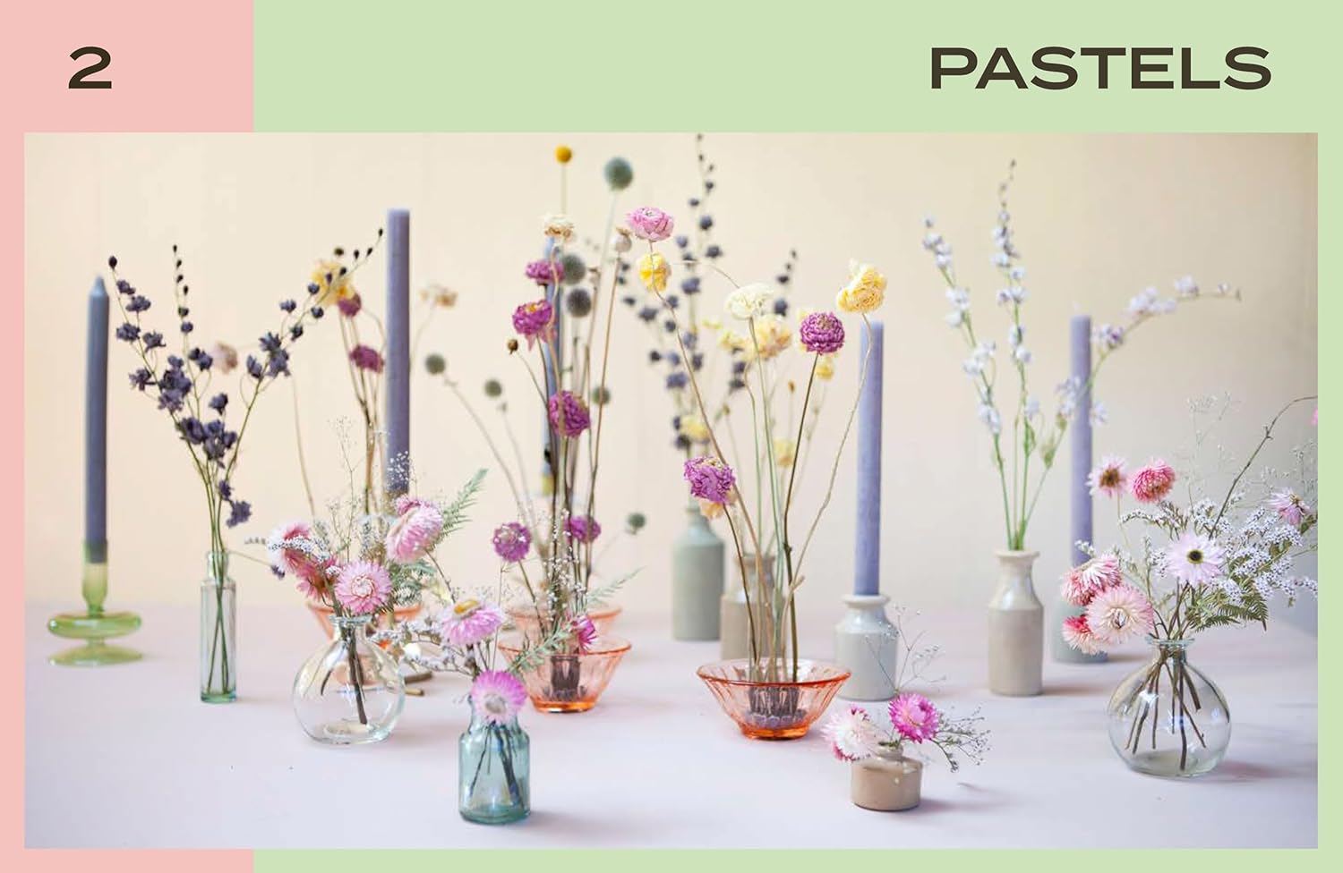 Decorative arrangement of flowers and candles in pastel colors on a neutral background.