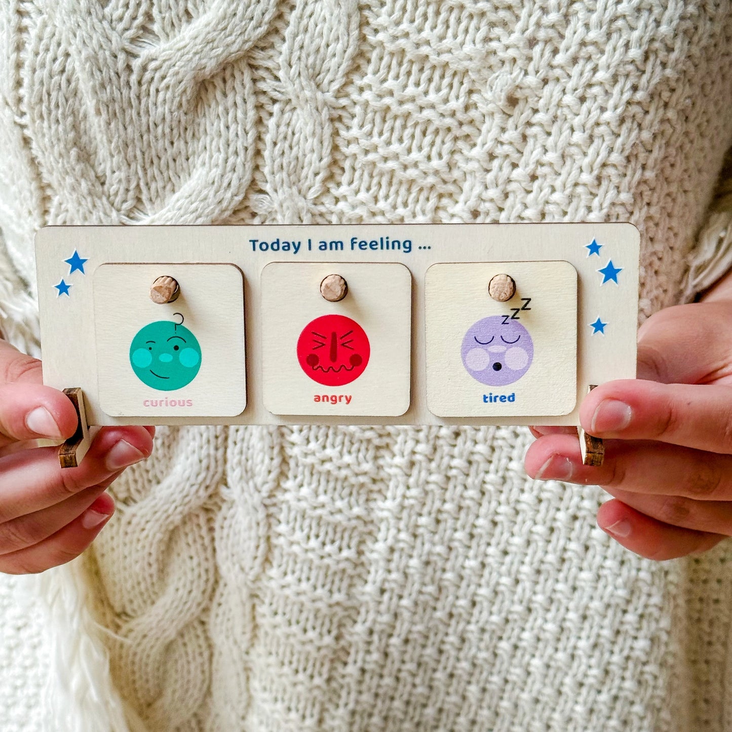 Wooden emotion chart held by hands against a knitted background