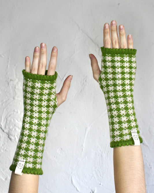 A pair of green and cream gingham knit fingerless gloves worn on hands, shown against a textured light gray background.