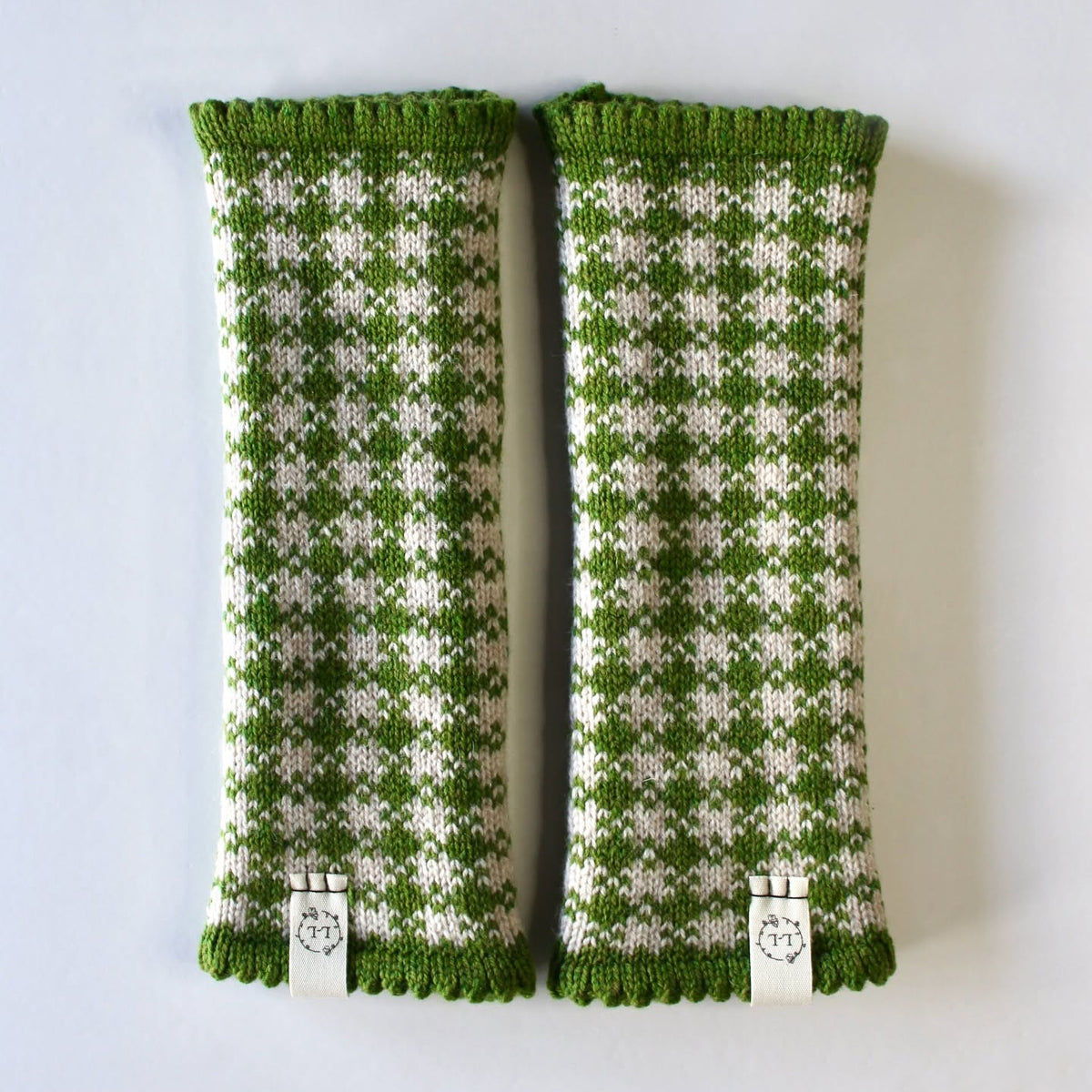 A pair of green and off-white patterned knit leg warmers with green ribbed cuffs and silver metal clips, displayed flat against a light gray background.