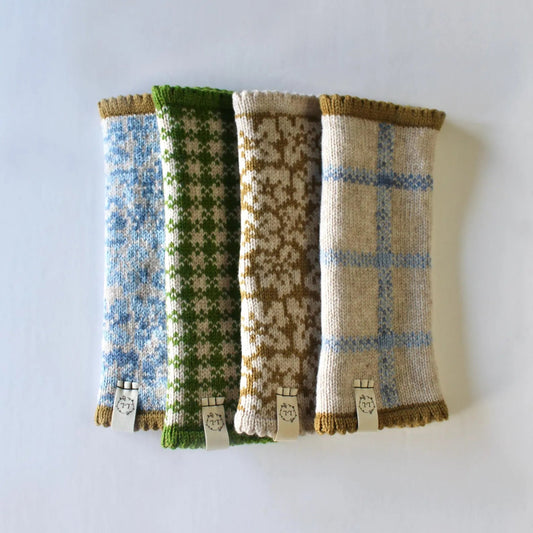 Four knitted lambswool fingerless gloves / wrist warmers,  with different knit patterns in blue, green, tan, and cream, arranged side-by-side on a plain white background.