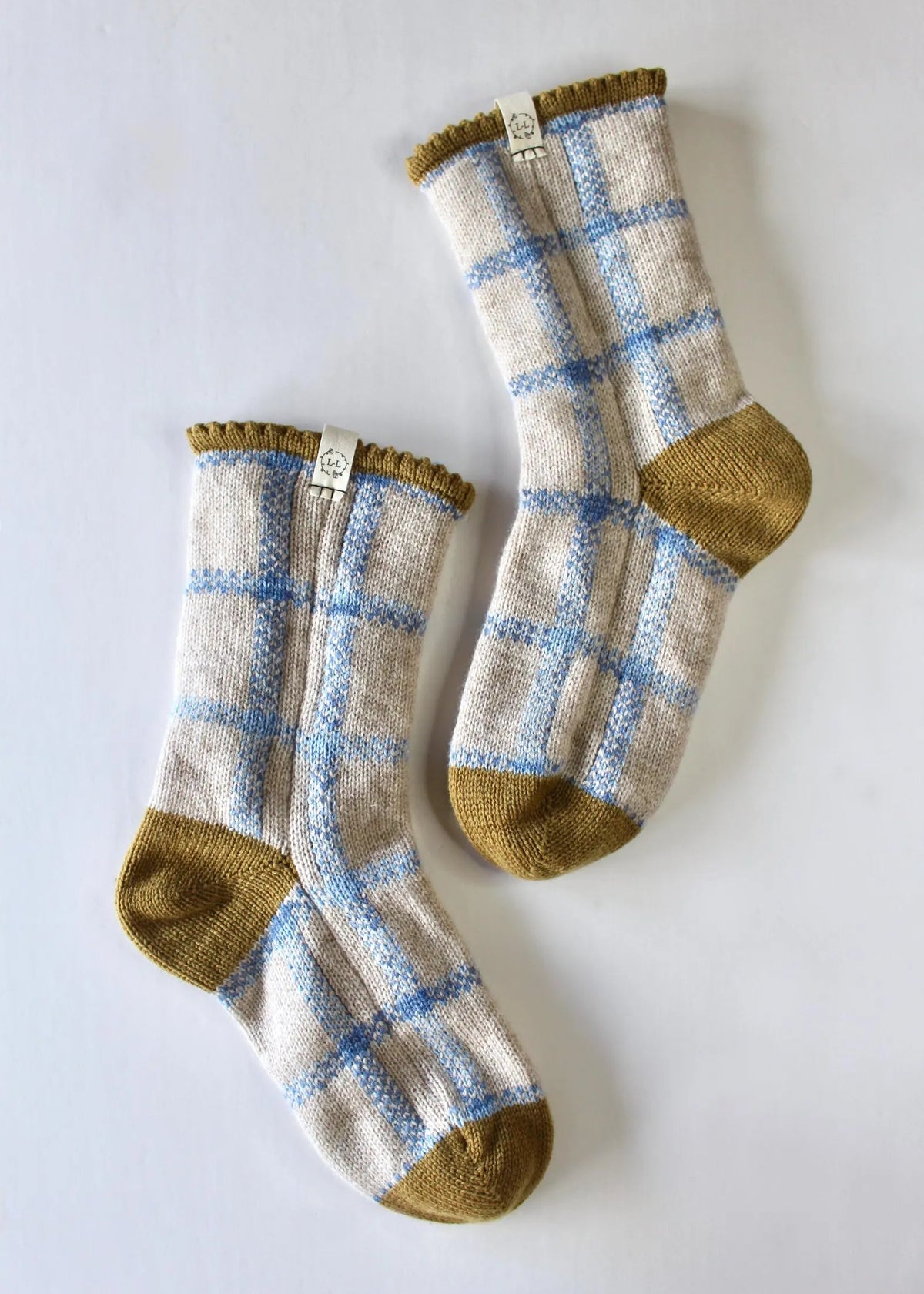 A pair of knit bed socks with a blue and oatmeal plaid pattern, light blue grid lines, and dijon yellow heels, toes, and cuffs, displayed on a light gray background.