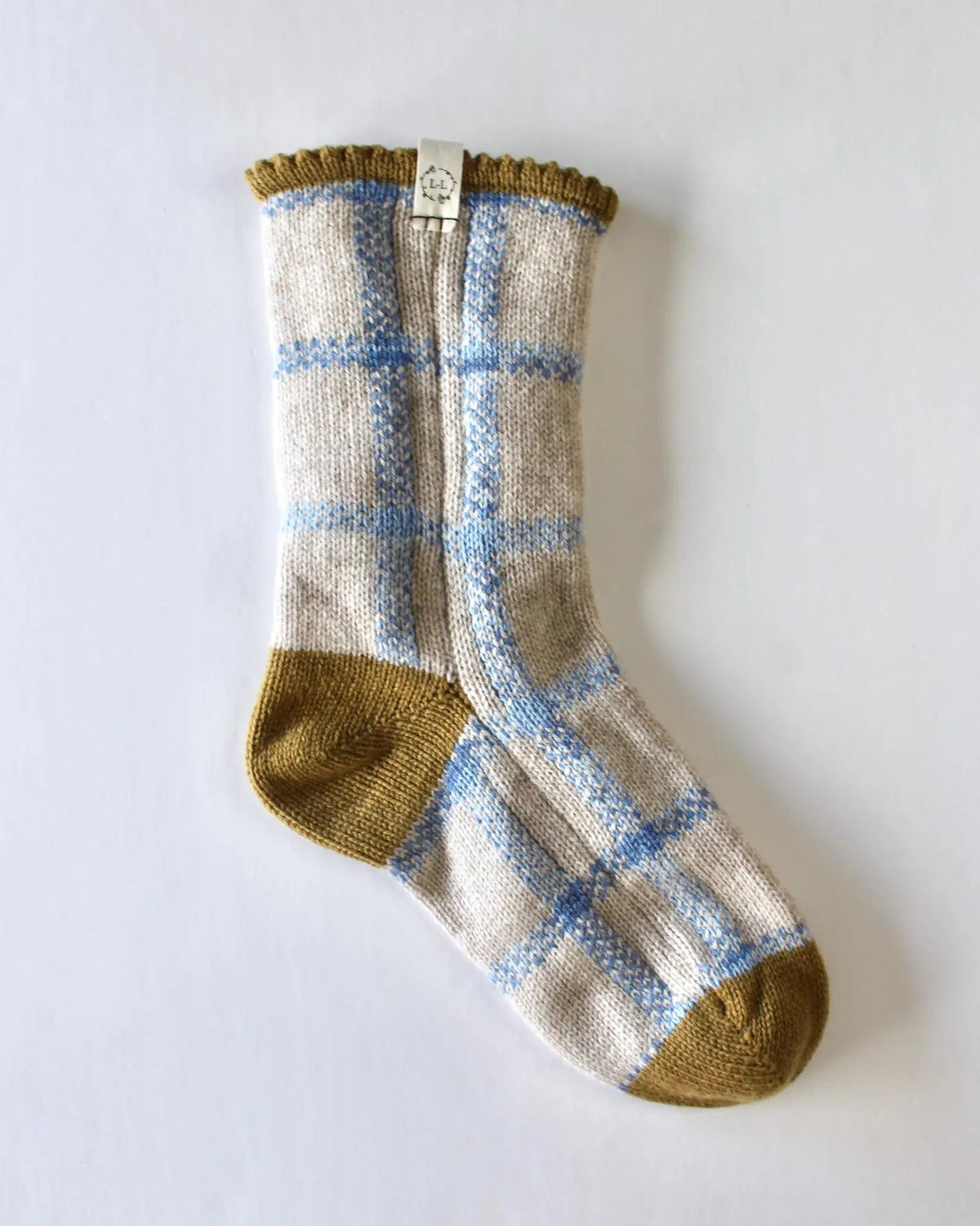 A single knitted sock with a cream base, light blue windowpane plaid pattern, and mustard yellow toe and cuff, displayed on a clean white background.