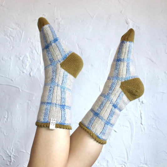Models legs wearing blue and cream ginham bed socks, against a textured white wall.