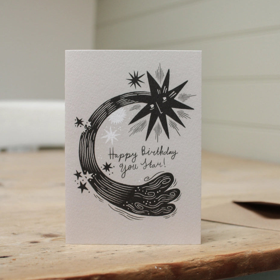 Greeting card with celestial design and 'Happy Birthday, you star!' text on a wooden surface.