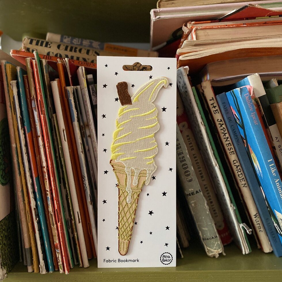 Fabric bookmark shaped like an ice cream cone on a card, surrounded by books