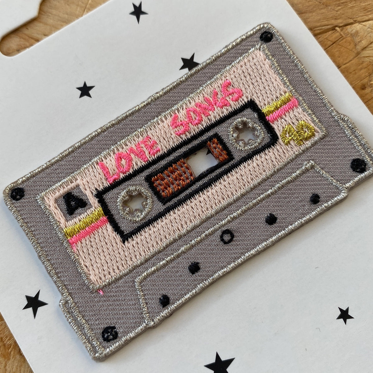 A closeup of a grey Love Songs mix tape patch on a white backing card.